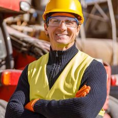 joyful-male-engineer-standing-by-tractor-at-factor-B54T3VP.jpg